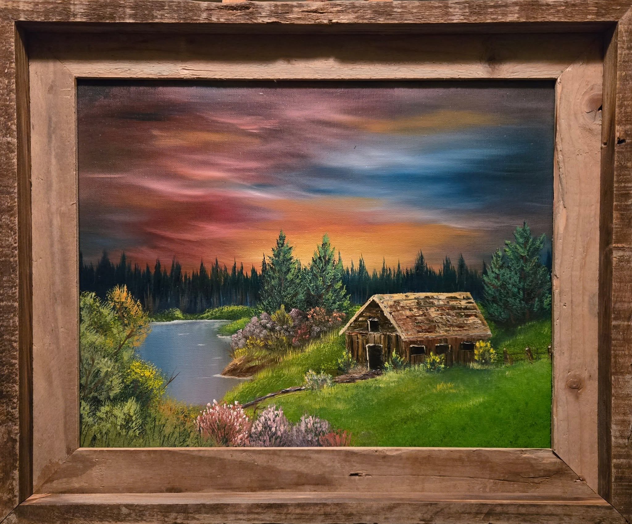 Framed oil painting of a sunset over a river with a rustic cabin